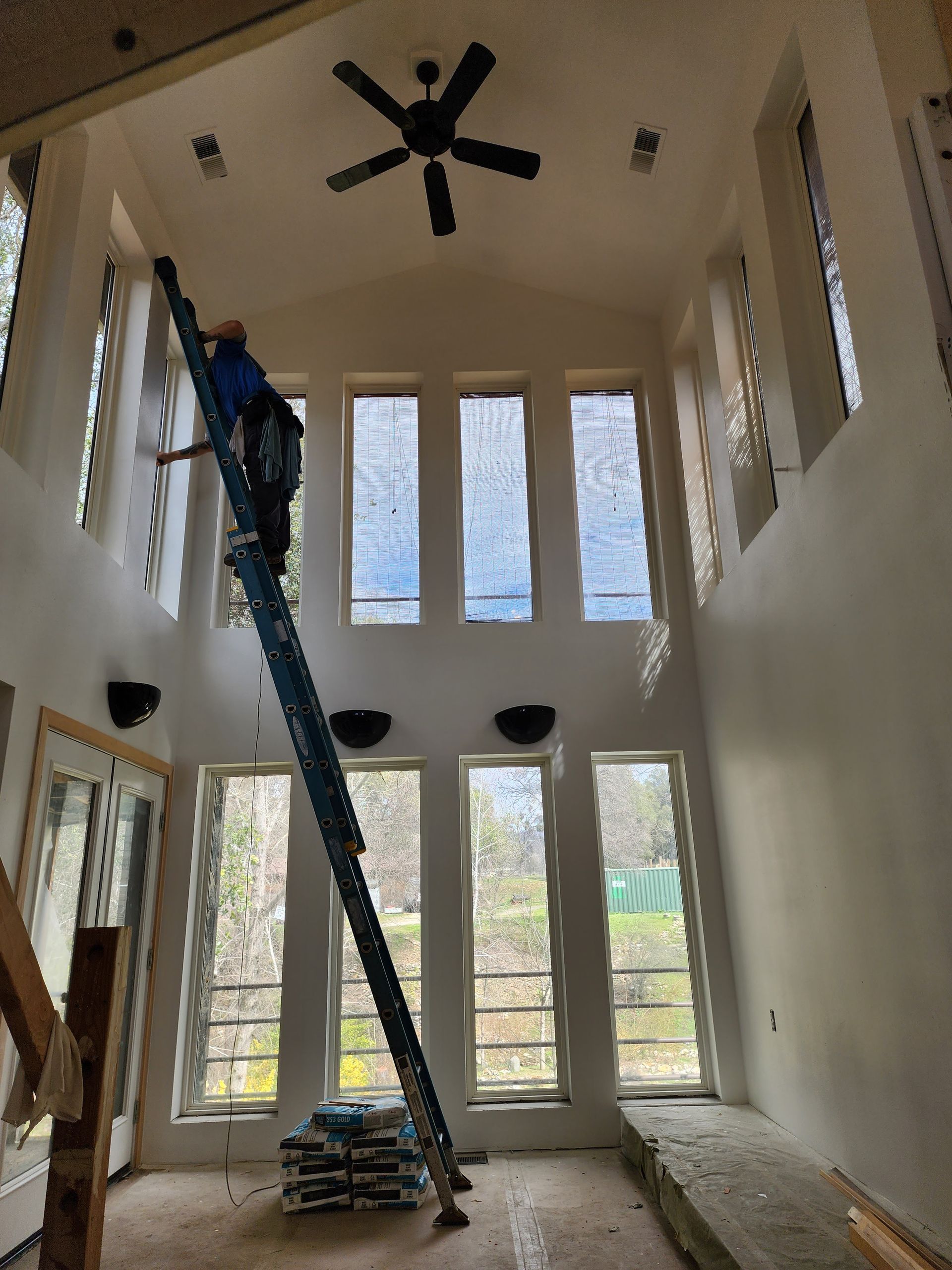 A man on a ladder in a room with a ceiling fan