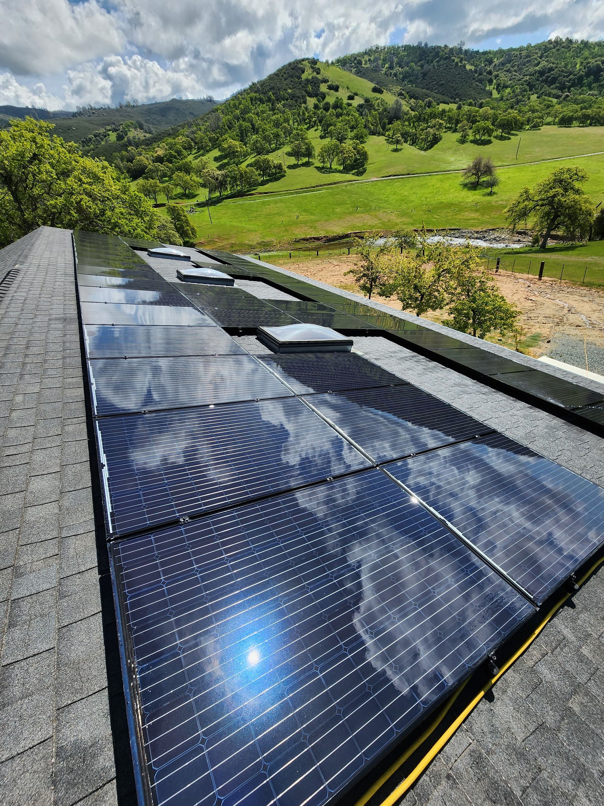 A row of solar panels on top of a roof with mountains in the background.