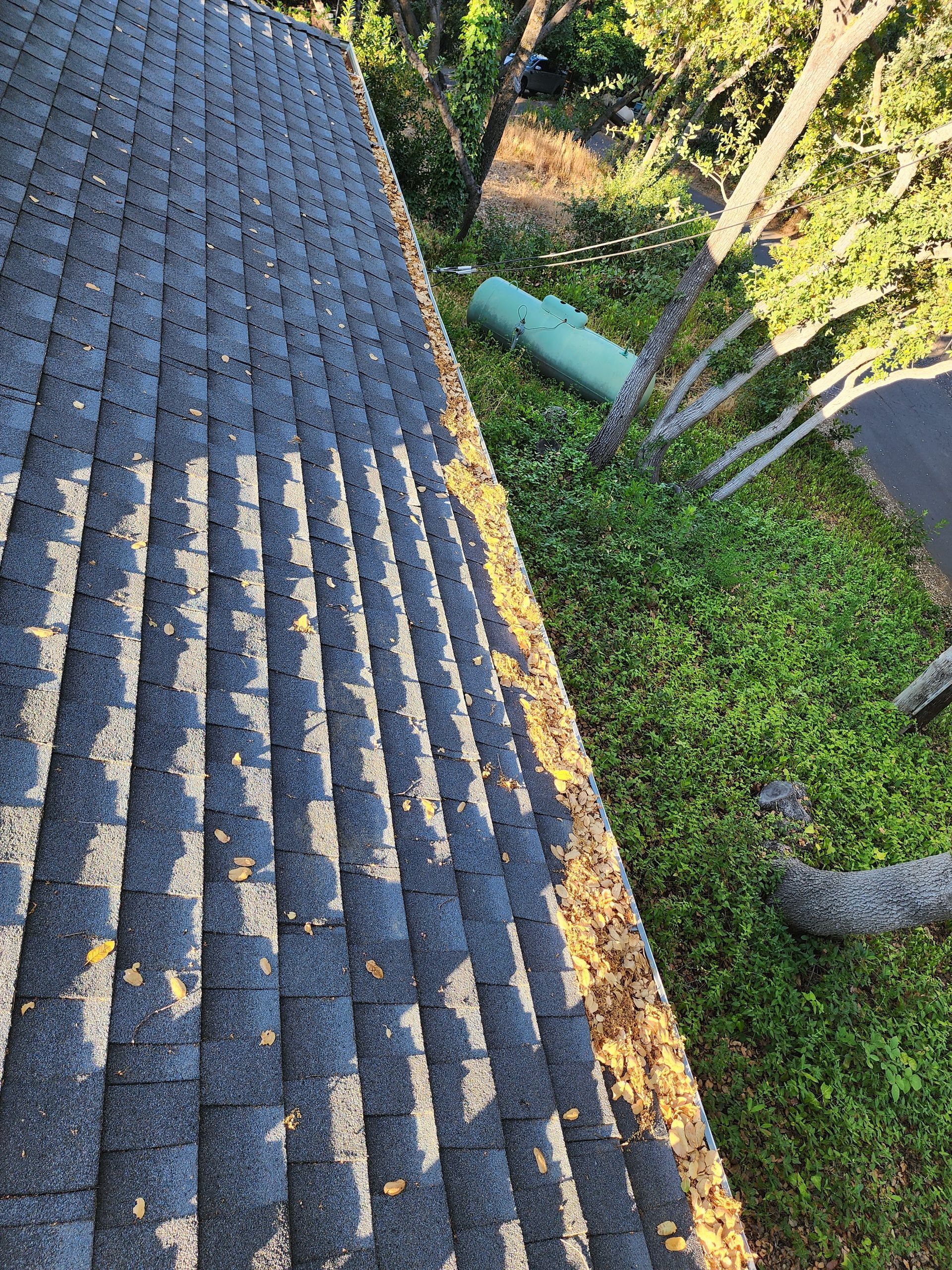 The roof of a house is covered in leaves and gutters.