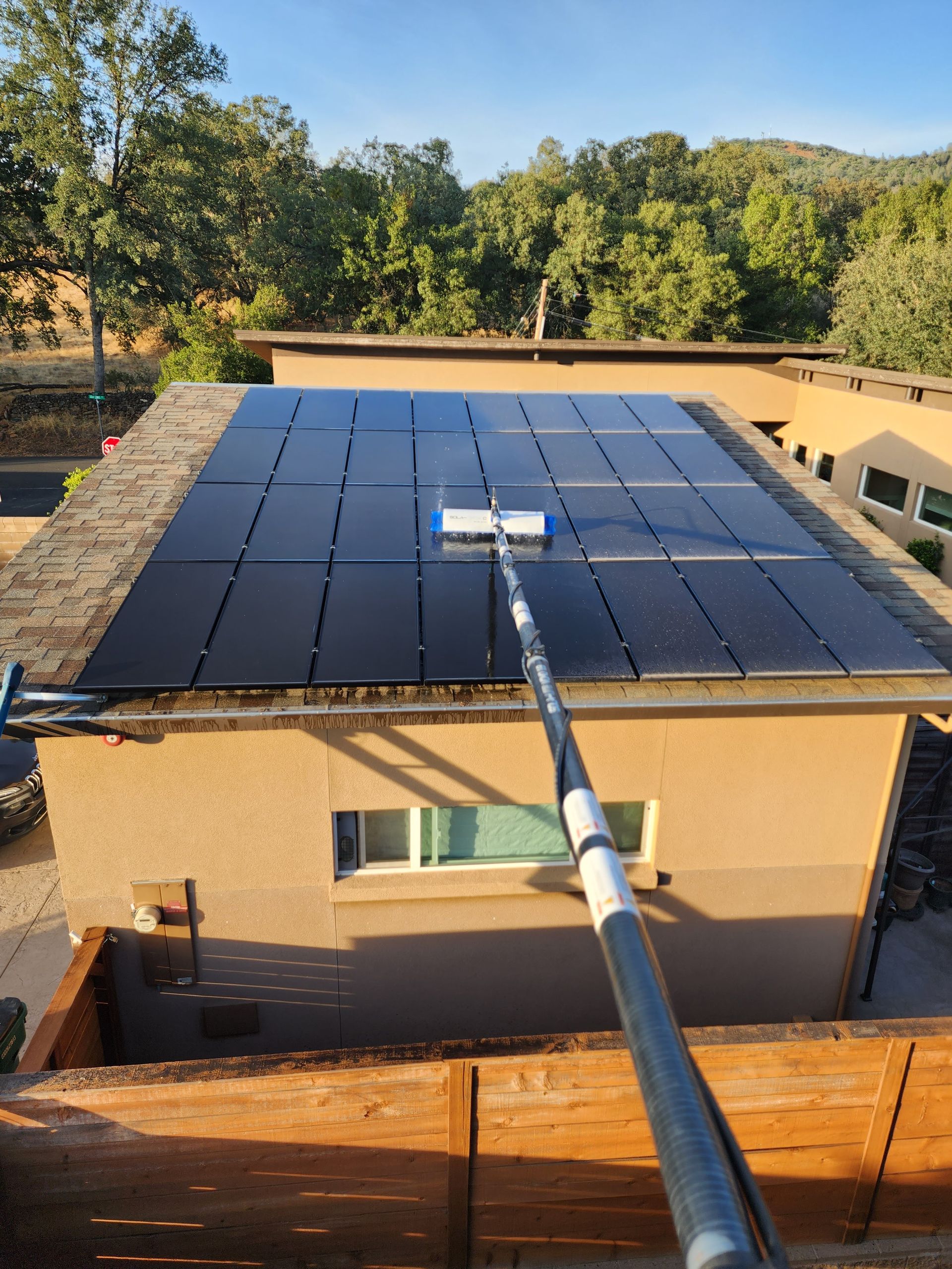 A person is cleaning a solar panel on the roof of a house.