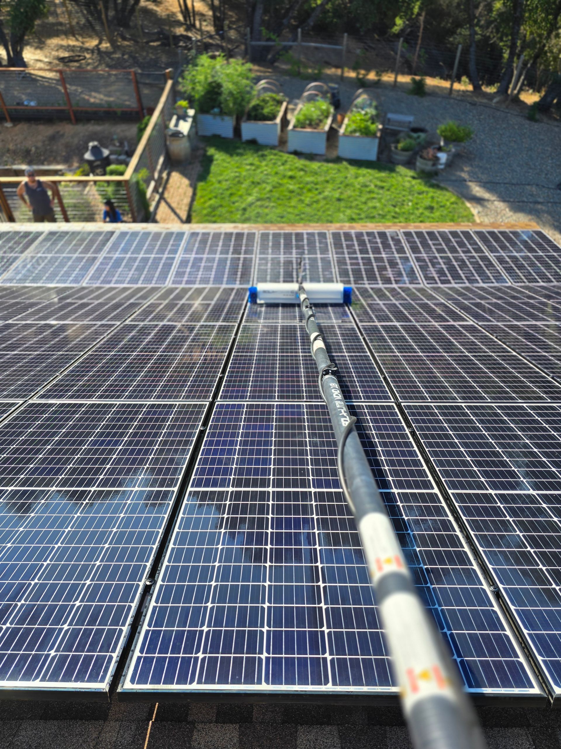 A person is cleaning solar panels on a roof with a brush.