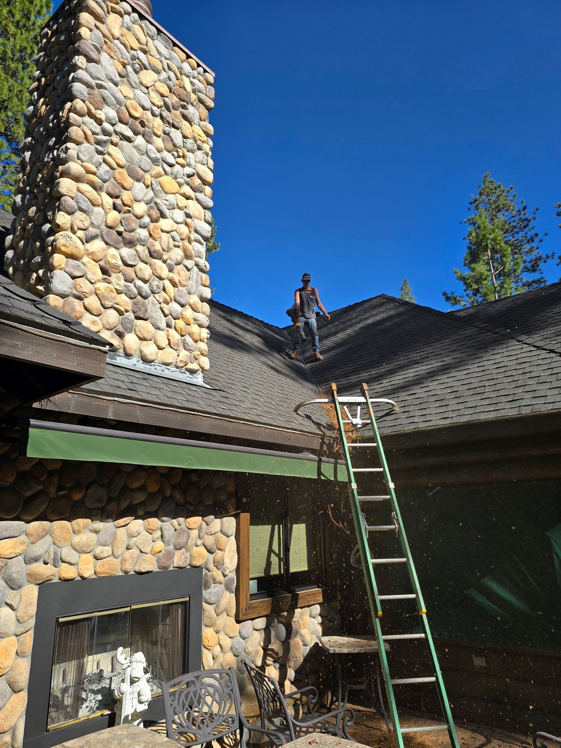 A man is standing on the roof of a house with a ladder.