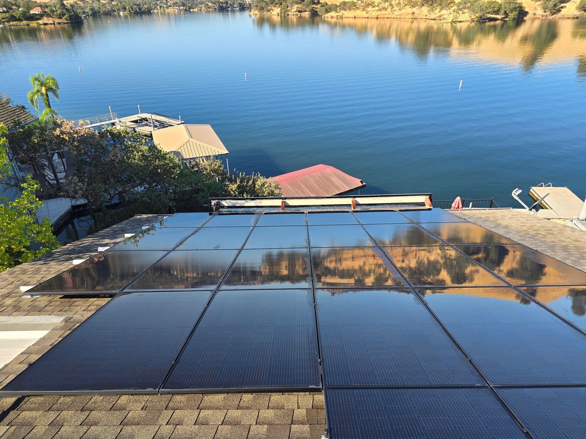A roof with solar panels on it overlooking a lake.