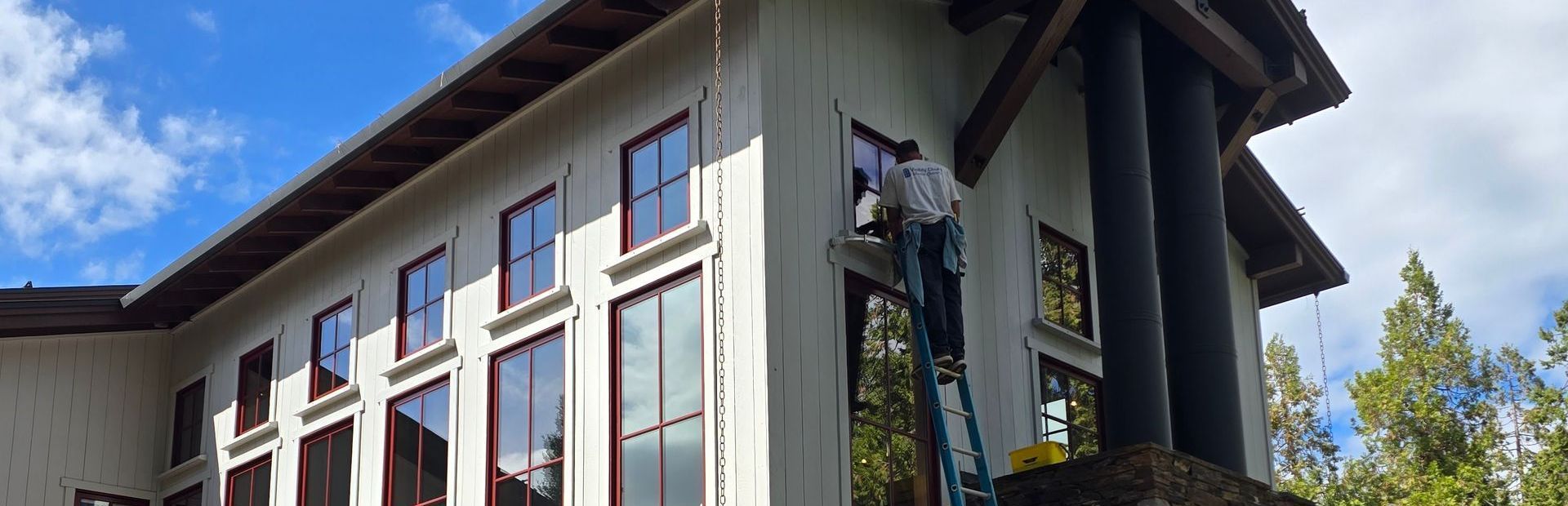 A man is painting the side of a large white house.