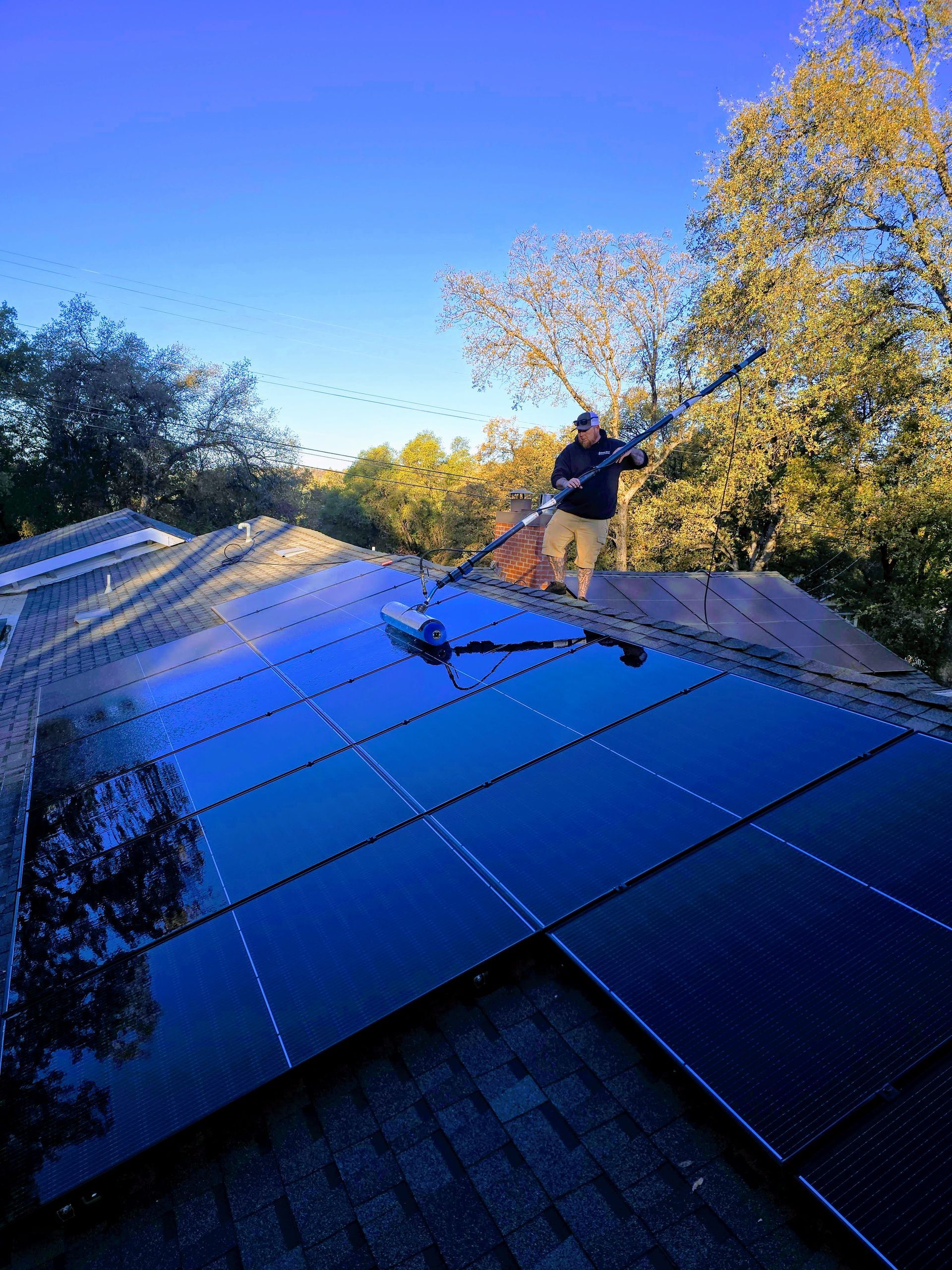 A man is cleaning solar panels on the roof of a house.