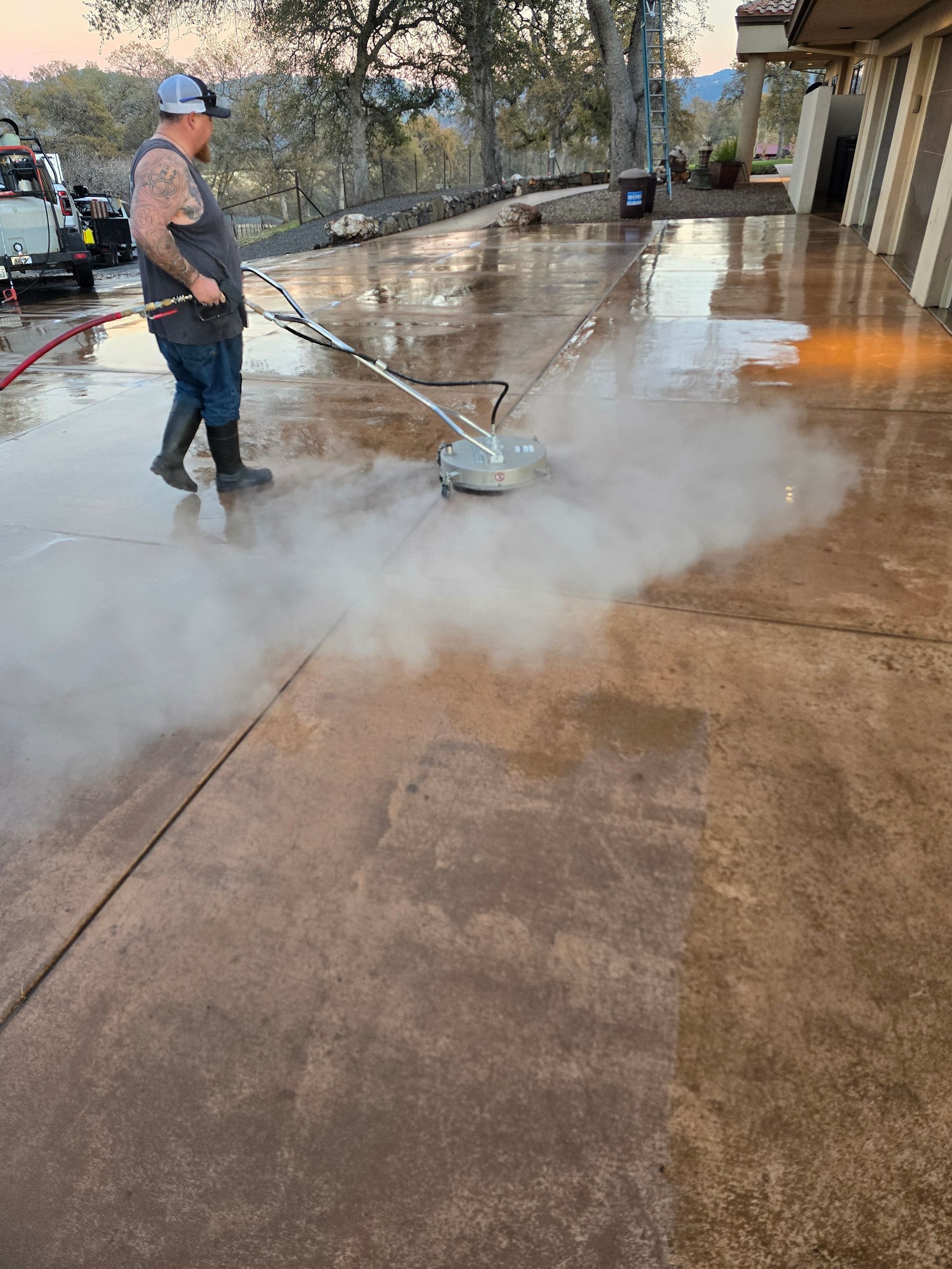 A man is cleaning a concrete driveway with a machine.