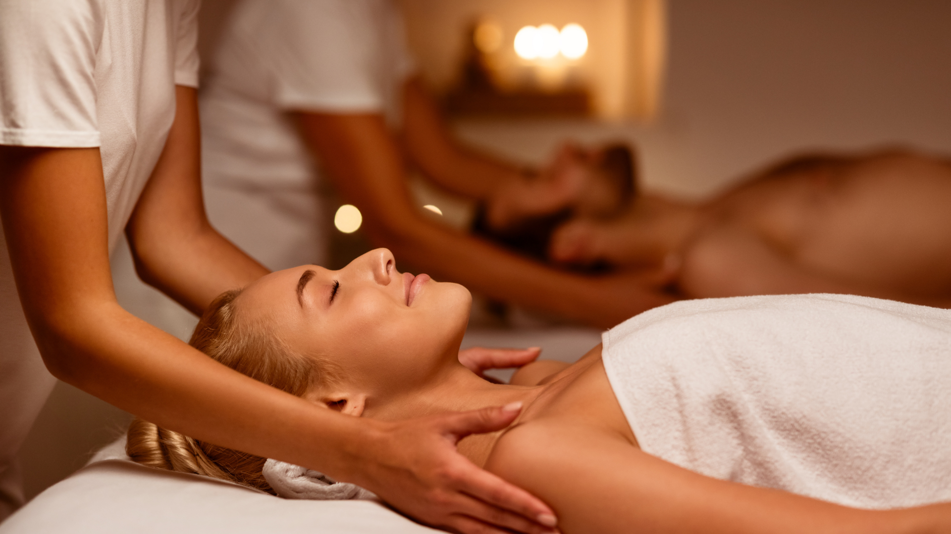 Woman receiving shoulder massage in spa; others in background.