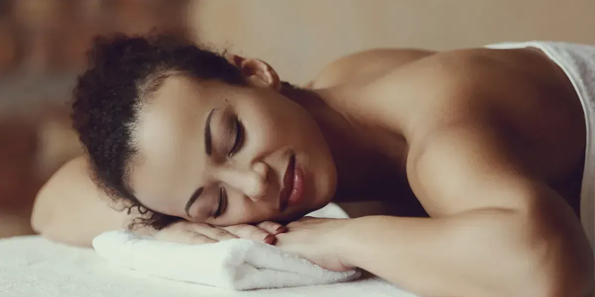 A woman with closed eyes rests her head on a towel during a massage, indoor setting.
