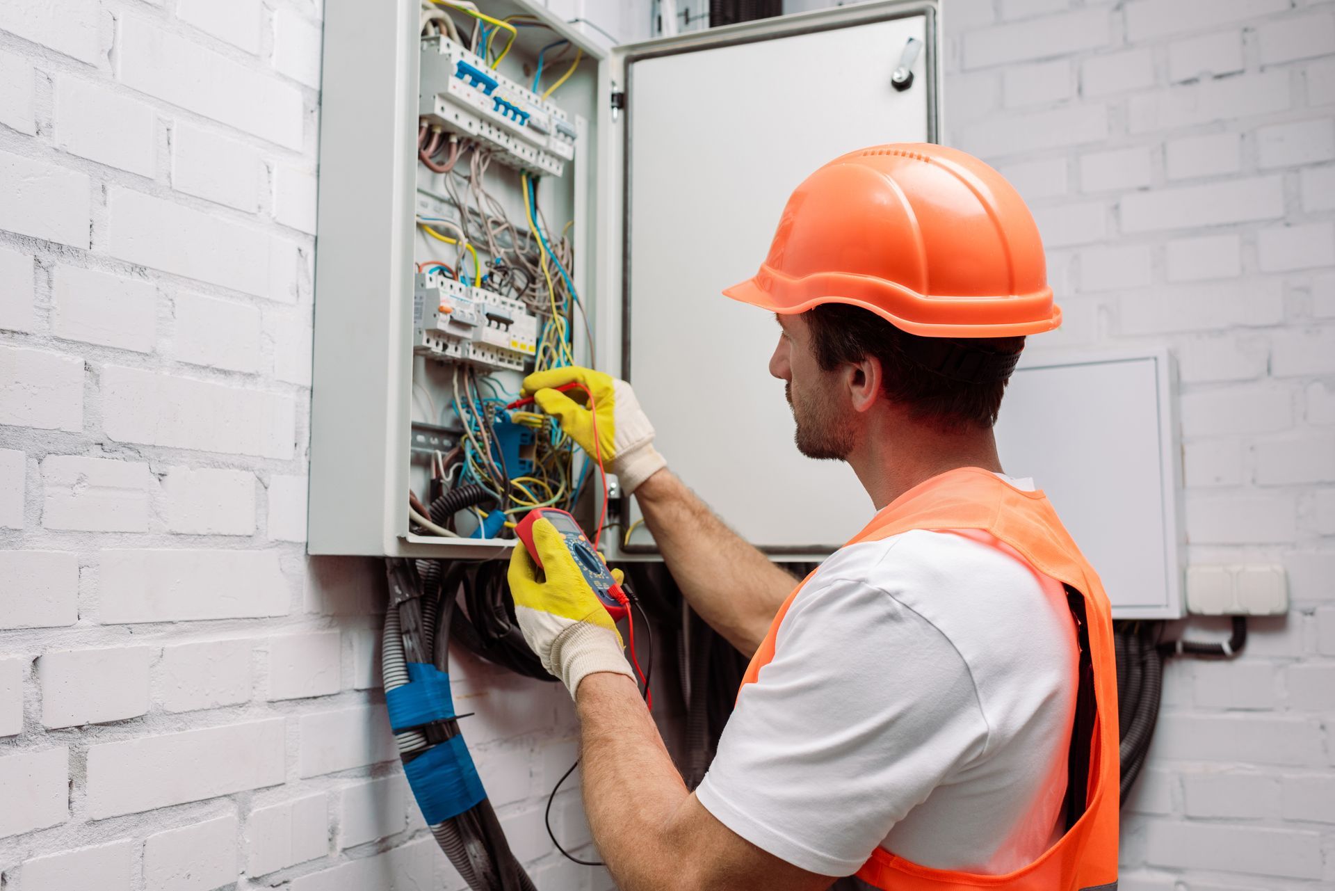 Electrician in safety gear working inside an open electrical panel.