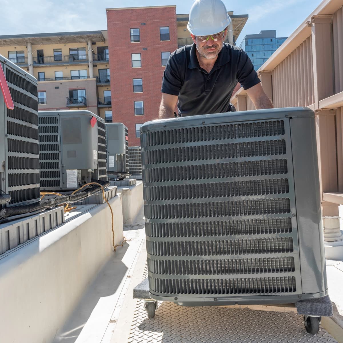 HVAC technician in a hard hat inspects rooftop air conditioning unit.