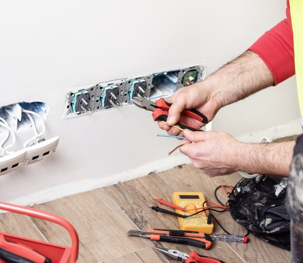 Electrician working on electrical wiring in a wall. Brown and blue wires, red tools.