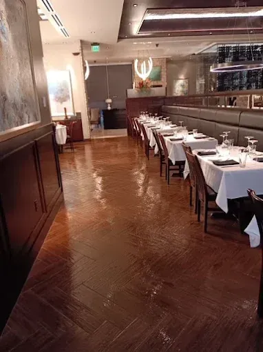 Empty restaurant dining room with white tablecloths, dark wood flooring and paneling.