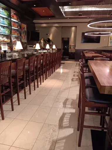 Bar area with wooden bar stools, tables, and ambient lighting. Tile floor.