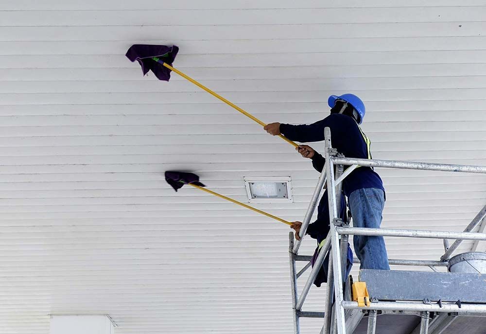 Person on scaffolding cleaning ceiling with two long-handled dusters.