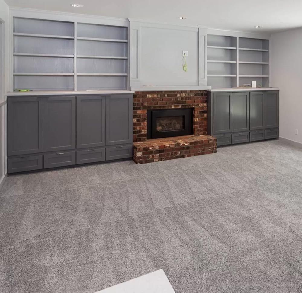 Gray-carpeted room with fireplace and built-in bookshelves. Fireplace has a brick surround and gray cabinets below.