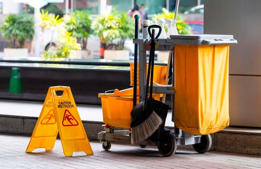 Yellow cleaning cart, caution sign, and plants in a lobby.