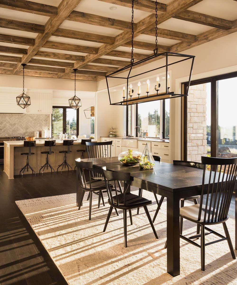 Dining room with dark table, black chairs, rug, and exposed wooden beams on ceiling.