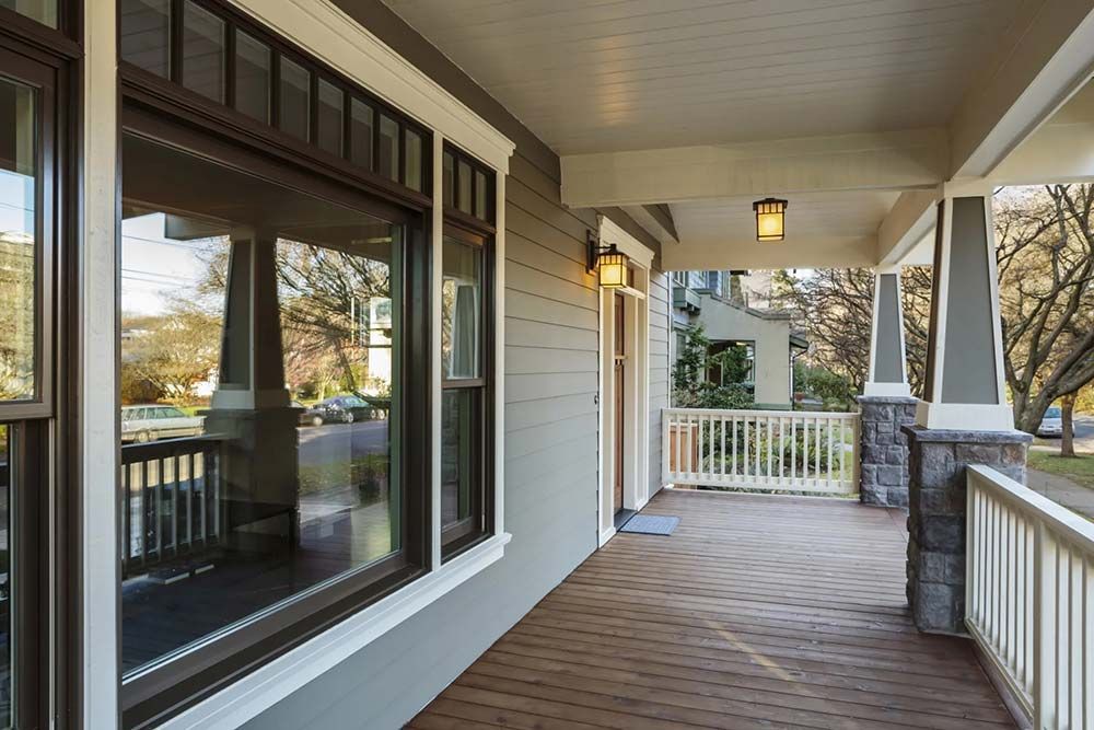Covered porch of a house with gray siding, columns, and a wooden floor.