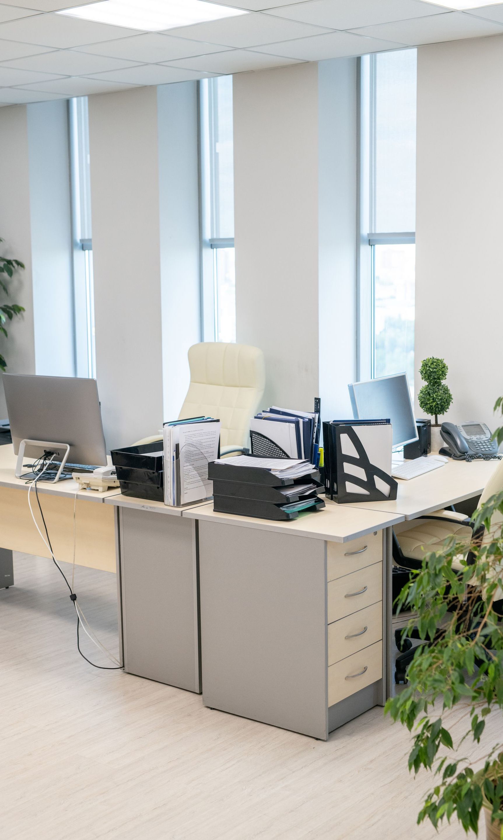 Office cubicle with desks, computers, and documents near a window.