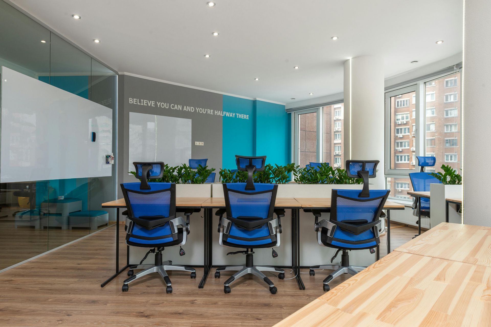 Office with blue chairs, whiteboards, plants, and wooden desks.