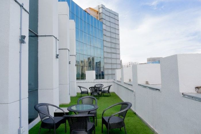 Rooftop patio with black wicker furniture on green turf, white pillars and building in the background against a blue sky.
