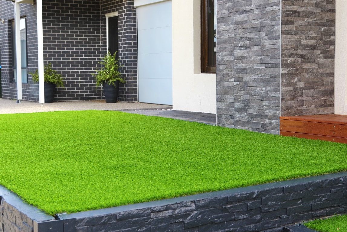 Lush green artificial turf in front of a modern home with black brick and stone accents.