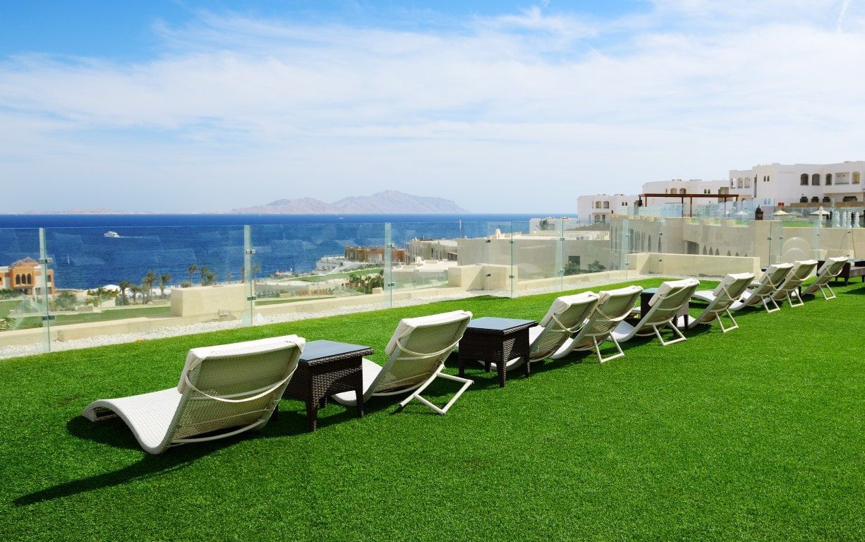 Row of lounge chairs on green artificial turf overlooking the ocean.