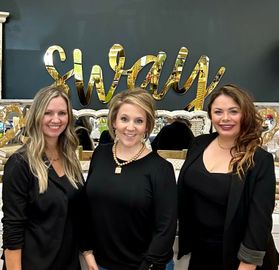 Three women are posing for a picture in front of a sign that says swan.