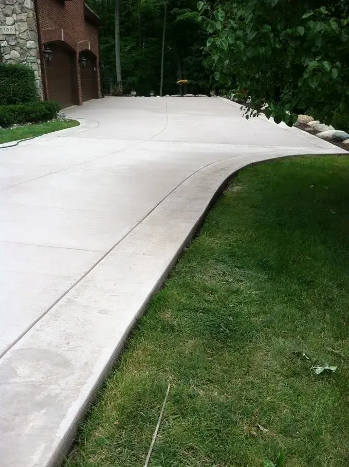 Concrete driveway curves alongside a green lawn, leading toward a house with two garage doors.