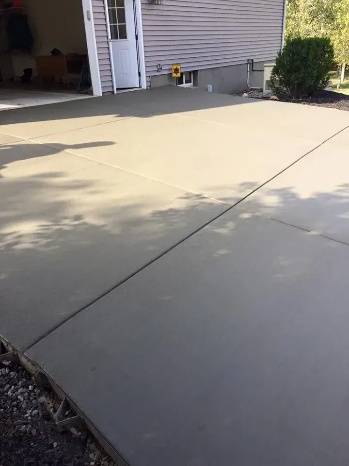 Newly poured gray concrete driveway next to a light-colored house.