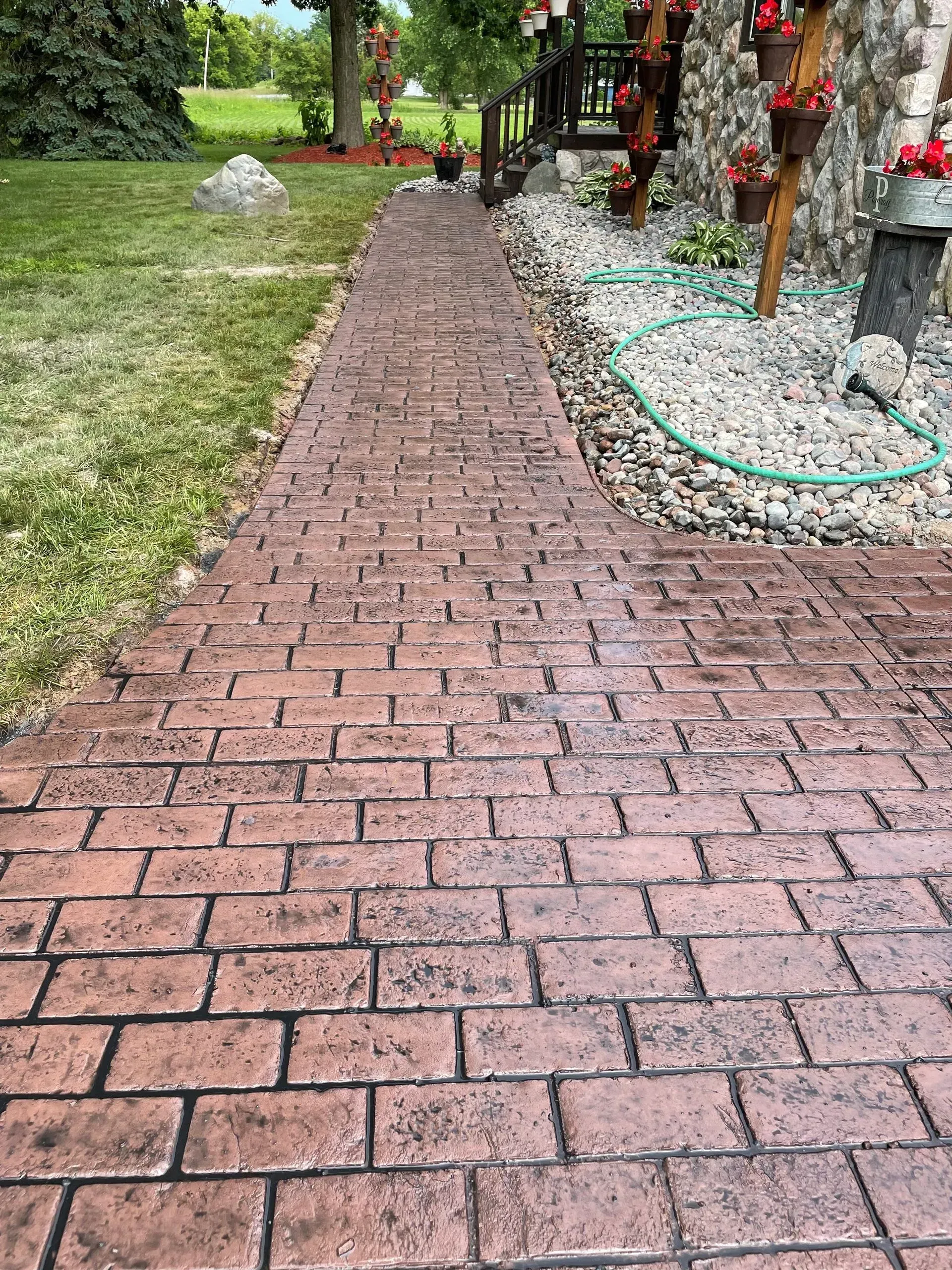 Brick-patterned walkway leading from green lawn to building with flower pots.