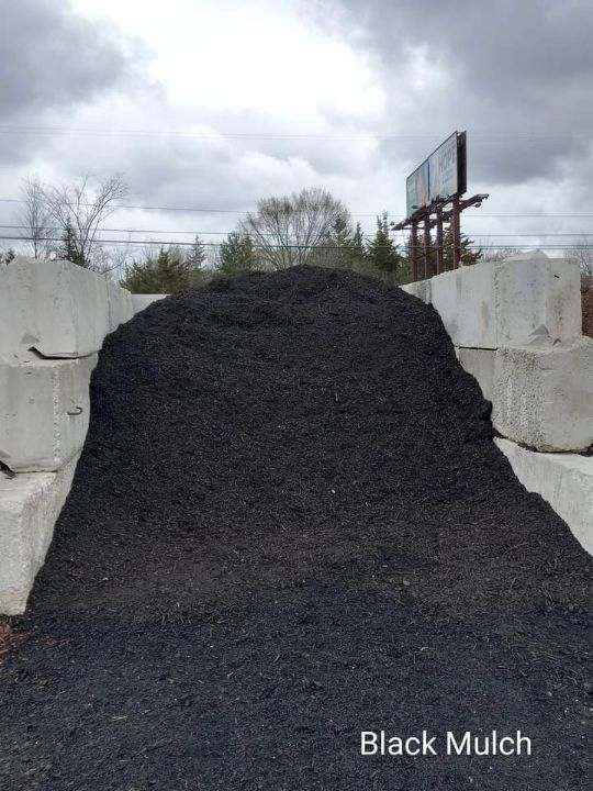 Pile of black mulch contained by concrete blocks, under a cloudy sky.