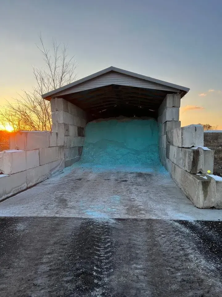 Salt shed filled with blue-tinted road salt, blocks of concrete forming the structure, in front of a setting sun.