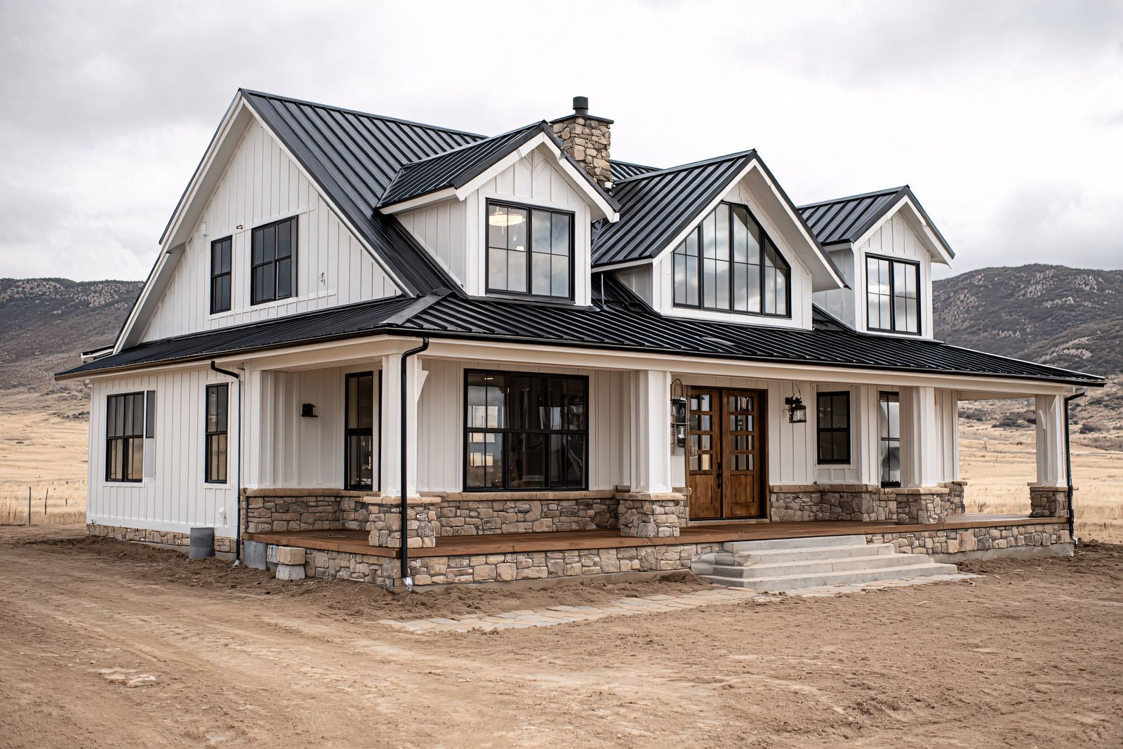 White farmhouse with black roof and trim, stone accents, and covered porch, set in a dry, open landscape.