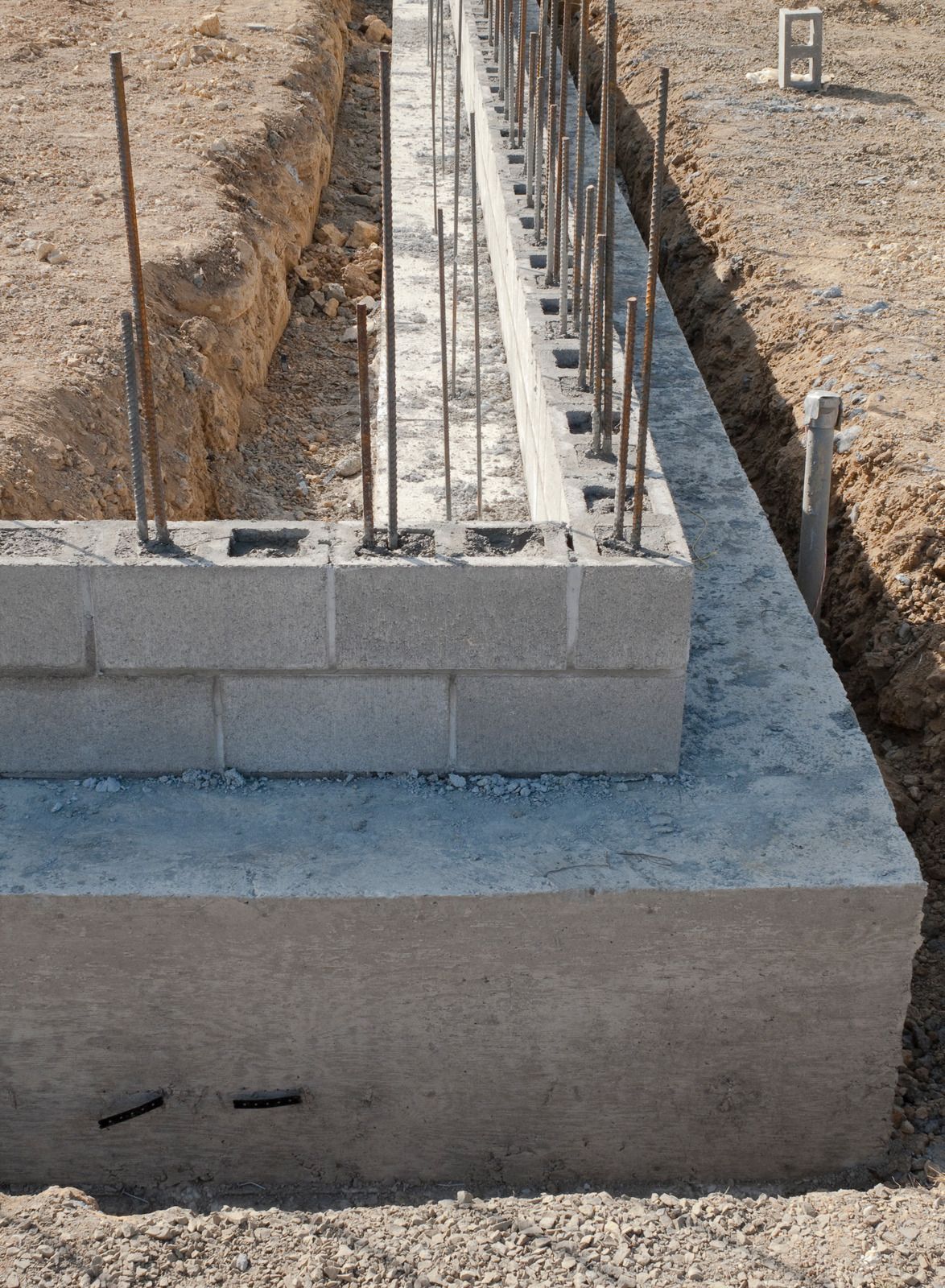 Foundation construction: concrete base with cinder blocks and rebar in an excavated trench.