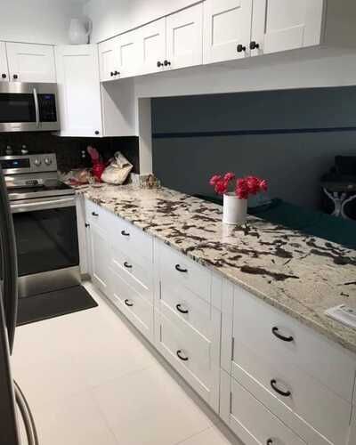 Modern white kitchen with black appliances and marble countertop, featuring a vase of pink flowers.