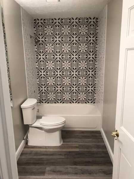 Small bathroom with a toilet, bathtub, dark wood floor, and patterned accent wall.