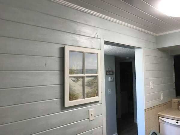 Gray-paneled interior wall with a small framed window and a doorway leading to a dark hall