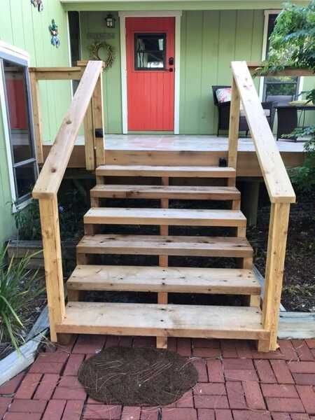 Front porch stairs with wooden railings leading to a red door on a green house