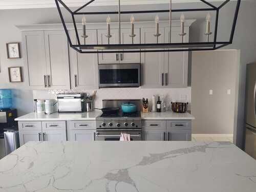 Modern kitchen with gray cabinets, stainless steel appliances, and a large white marble island
