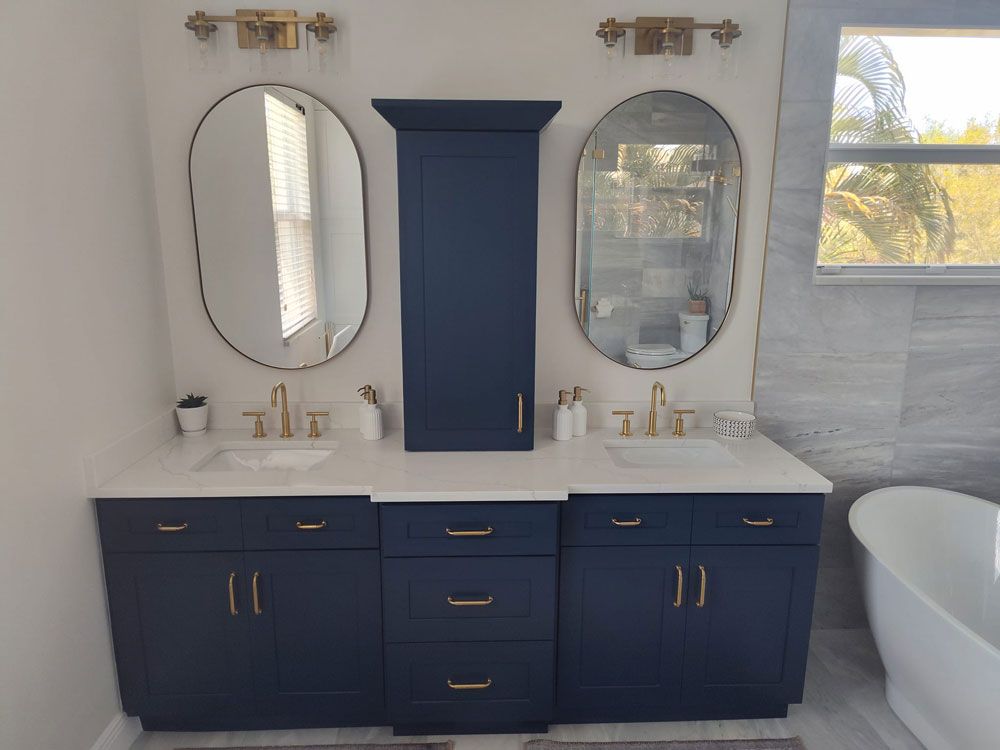 Blue double vanity with oval mirrors in a bright bathroom, with a freestanding tub on the right