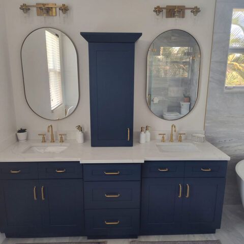 Modern bathroom vanity with navy cabinets, white countertops, twin oval mirrors, and brass fixtures.