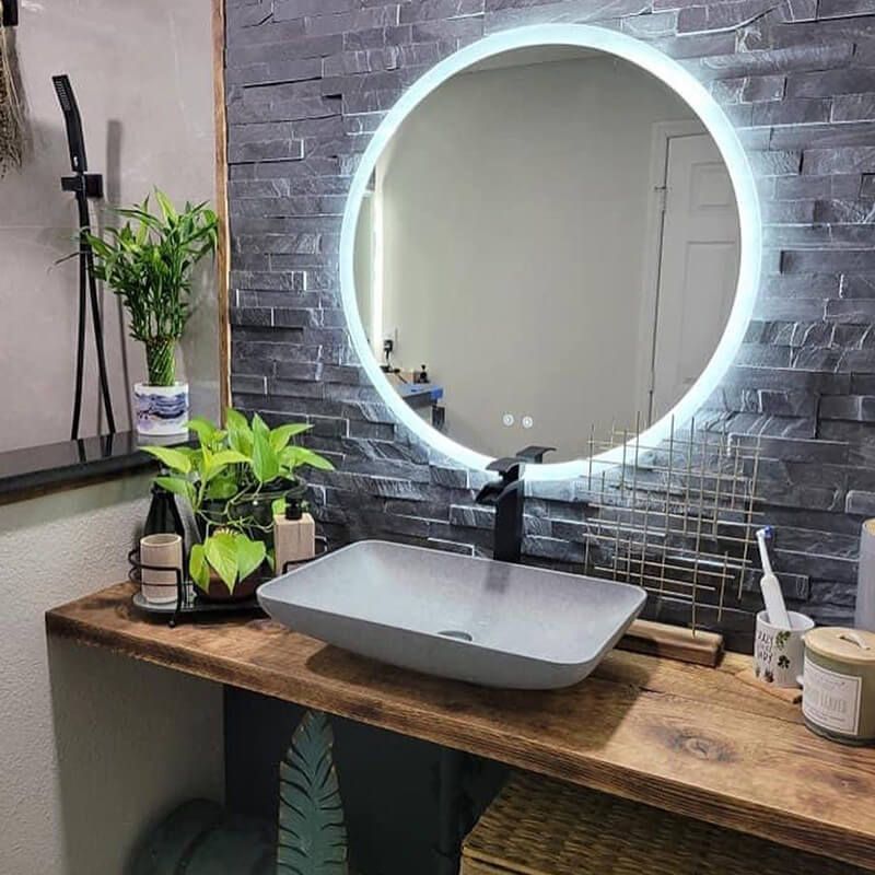Modern bathroom vanity with round backlit mirror, gray vessel sink, and potted plants on a wood counter