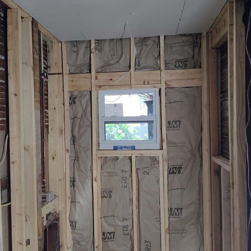 Unfinished room with insulation-lined walls and a small window centered on the back wall