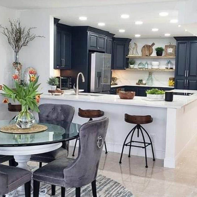 Modern kitchen with navy cabinets, white island, and a glass dining table in the foreground