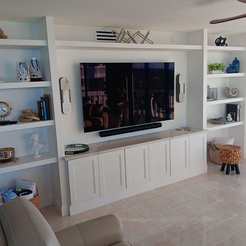 Living room wall with mounted TV, white shelving, and built-in cabinet in a bright, tiled space