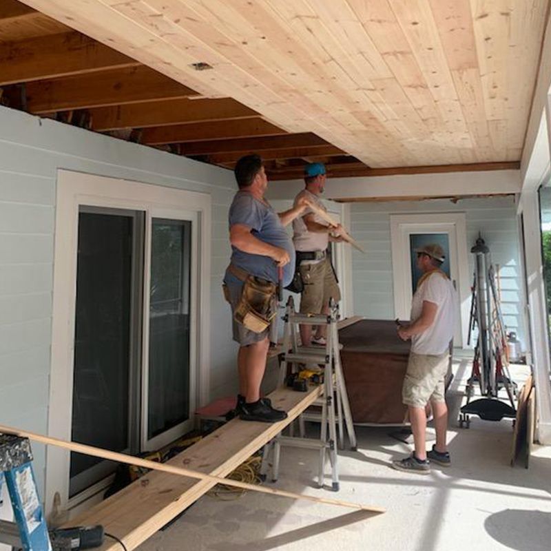 Workers building a porch ceiling and railing on a covered patio with ladders and tools