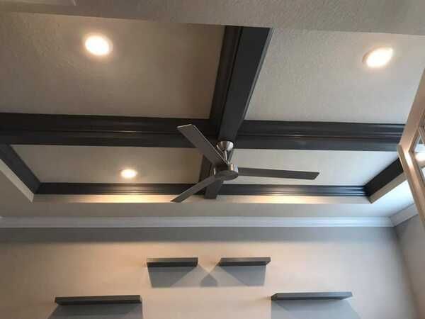 Ceiling with recessed lights, a fan, and dark geometric beams in a gray room