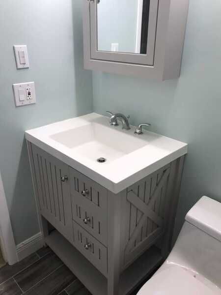 Small bathroom vanity with white sink, gray cabinet, mirror, and part of a toilet.