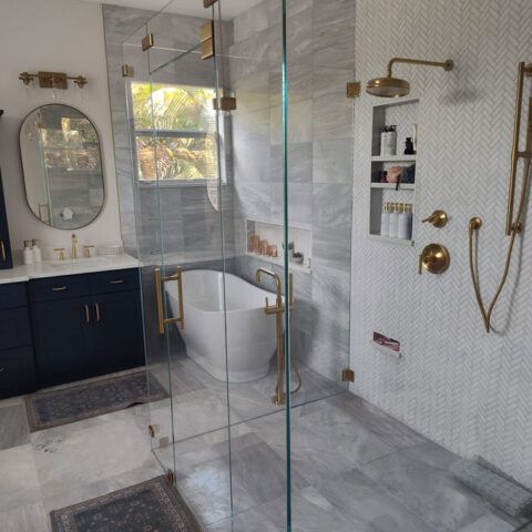 Modern marble bathroom with glass shower, gold fixtures, floating vanity, and oval mirror